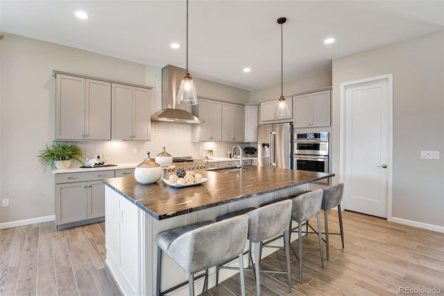 kitchen featuring stainless steel appliances, light hardwood / wood-style floors, an island with sink, and gray cabinetry