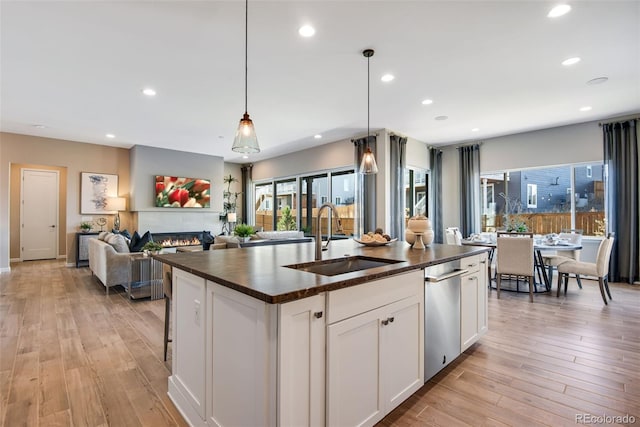 kitchen featuring white cabinetry, decorative light fixtures, sink, an island with sink, and light hardwood / wood-style flooring