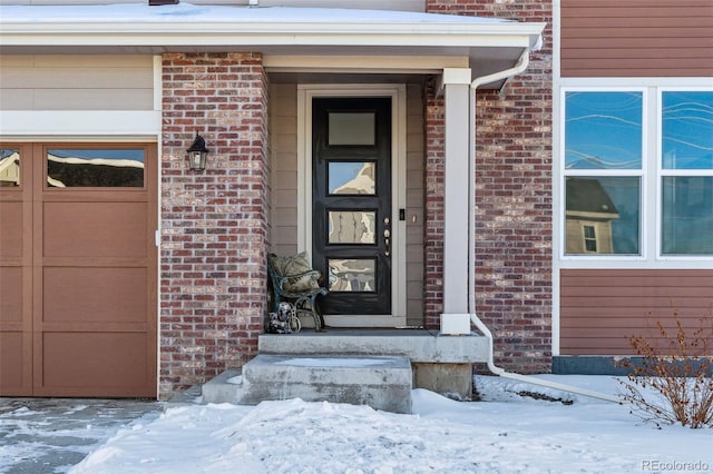 snow covered property entrance with a garage