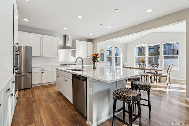 kitchen featuring lofted ceiling, sink, stainless steel appliances, a kitchen island with sink, and wall chimney range hood