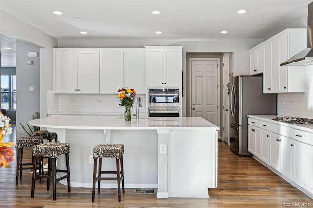 kitchen with wall chimney range hood, white cabinetry, a breakfast bar area, and a center island with sink