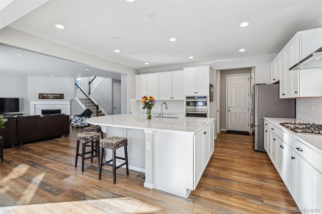 kitchen featuring sink, appliances with stainless steel finishes, a kitchen island with sink, tasteful backsplash, and white cabinets