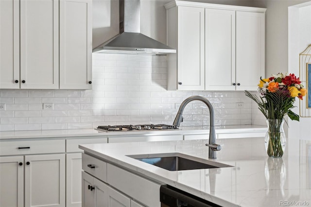 kitchen featuring sink, white cabinetry, wall chimney range hood, light stone countertops, and backsplash