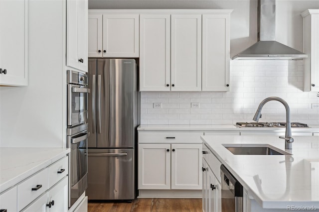 kitchen with appliances with stainless steel finishes, white cabinets, light stone counters, and wall chimney exhaust hood