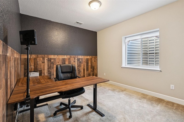 office space featuring light colored carpet, a textured ceiling, and wood walls