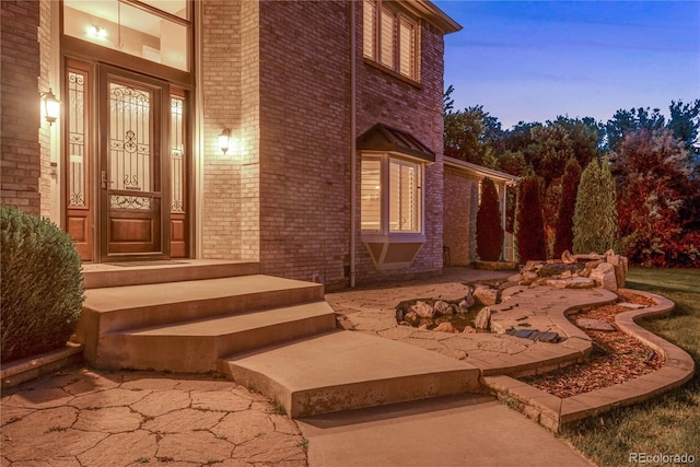 exterior entry at dusk featuring brick siding