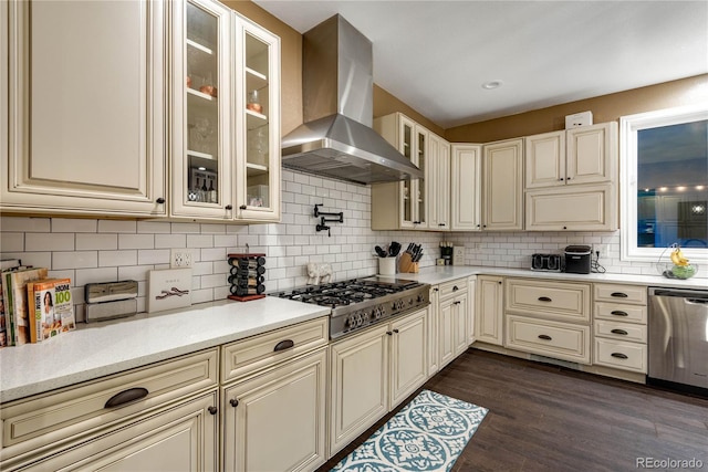 kitchen with decorative backsplash, wall chimney exhaust hood, appliances with stainless steel finishes, and cream cabinets