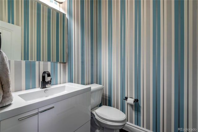 half bathroom featuring vanity, wallpapered walls, and toilet