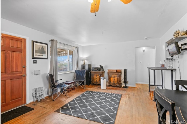 office area with baseboards, ceiling fan, a wood stove, and hardwood / wood-style flooring