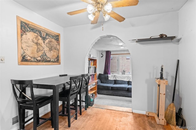 dining area featuring arched walkways, baseboards, a ceiling fan, and wood finished floors