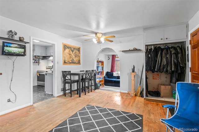 interior space with a ceiling fan, wood finished floors, arched walkways, and baseboards