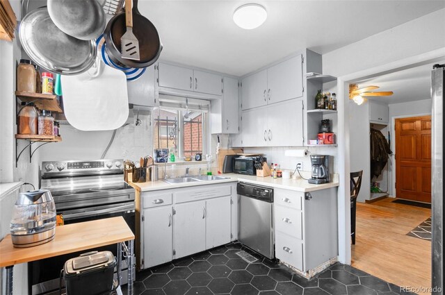 kitchen with open shelves, a sink, backsplash, appliances with stainless steel finishes, and light countertops