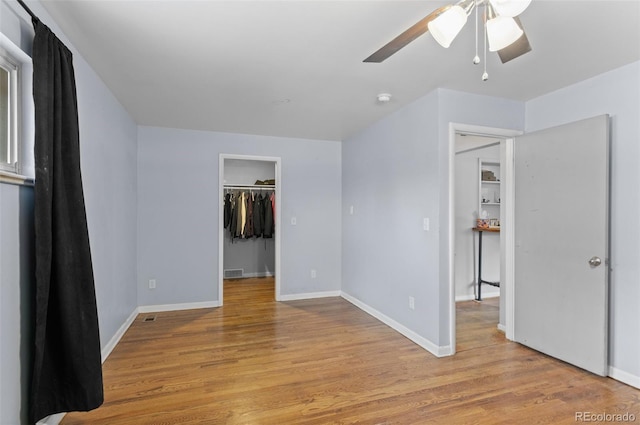 unfurnished bedroom with light wood-style flooring, a spacious closet, a ceiling fan, and baseboards