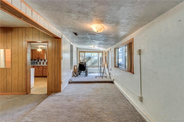 corridor featuring light carpet, a textured ceiling, wooden walls, and vaulted ceiling