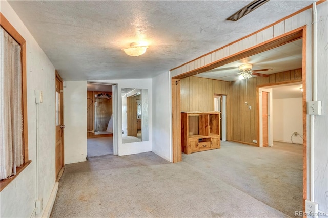 carpeted spare room featuring ceiling fan, a textured ceiling, and wood walls