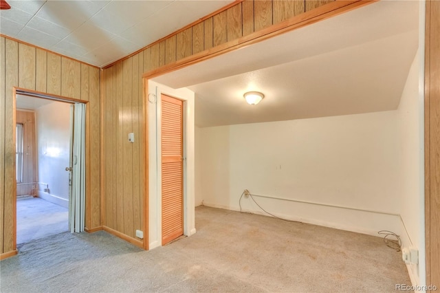 empty room featuring wooden walls, vaulted ceiling, and light colored carpet