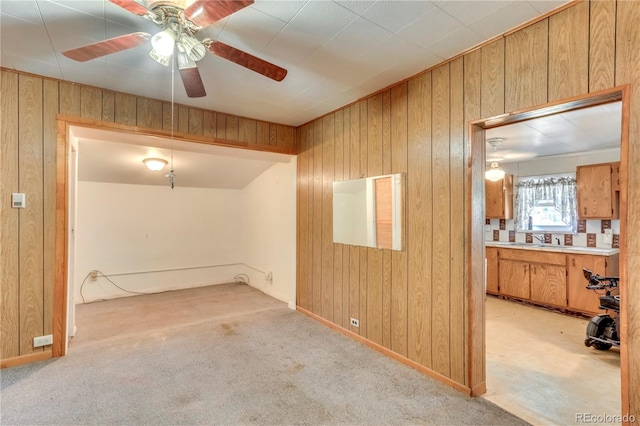 carpeted empty room with ceiling fan, wood walls, and sink