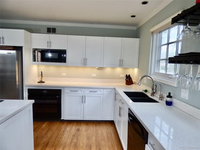 kitchen featuring visible vents, crown molding, white cabinetry, a sink, and black appliances