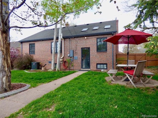back of property featuring a lawn, brick siding, fence, and central air condition unit