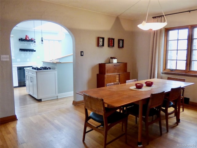 dining area featuring baseboards, arched walkways, and light wood finished floors