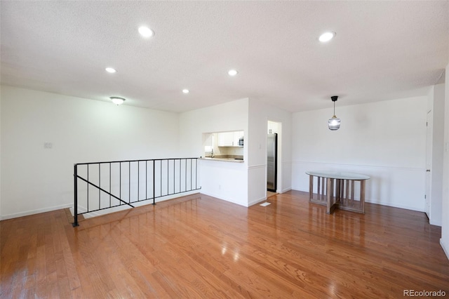 unfurnished room featuring light wood finished floors, baseboards, a textured ceiling, and recessed lighting