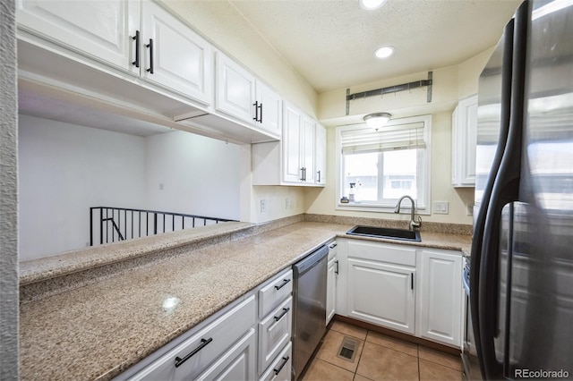 kitchen featuring a textured ceiling, light tile patterned floors, a sink, white cabinets, and appliances with stainless steel finishes