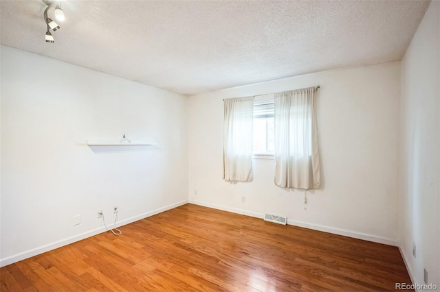 spare room featuring a textured ceiling, wood finished floors, visible vents, and baseboards