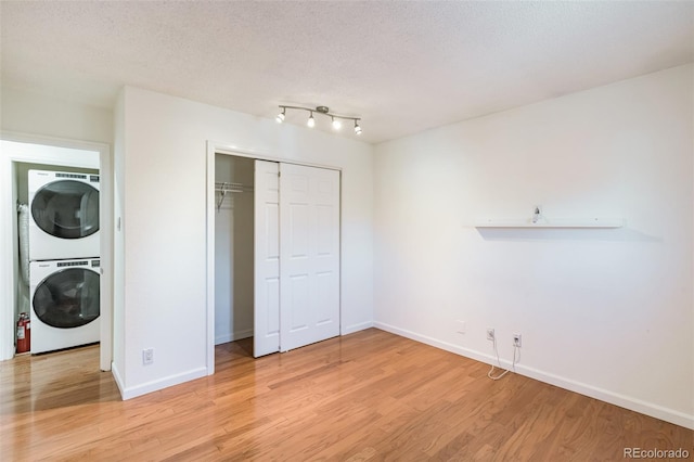 unfurnished bedroom with baseboards, stacked washer / dryer, light wood-style flooring, a textured ceiling, and a closet