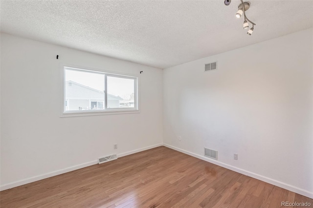 empty room featuring light wood finished floors, visible vents, and a textured ceiling