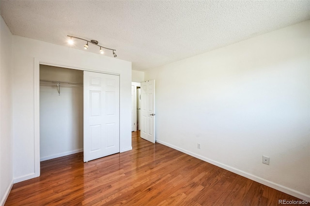 unfurnished bedroom with a textured ceiling, a closet, wood finished floors, and baseboards