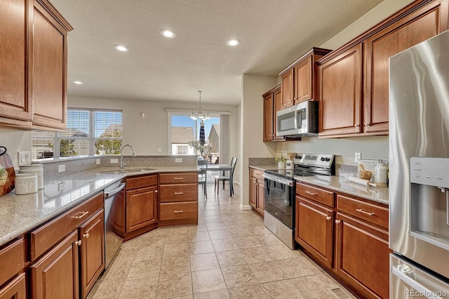 kitchen with light stone countertops, decorative light fixtures, stainless steel appliances, an inviting chandelier, and sink