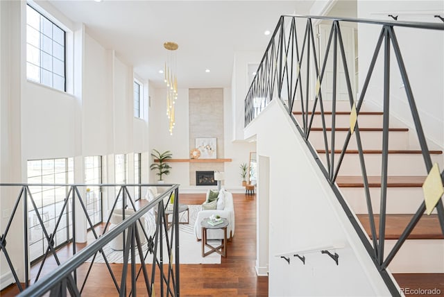 staircase featuring an inviting chandelier, wood-type flooring, a towering ceiling, and a tiled fireplace