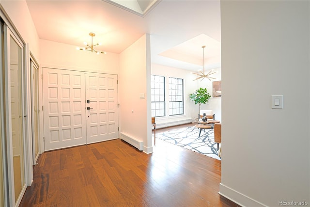 foyer entrance with a notable chandelier, a raised ceiling, wood-type flooring, and a baseboard heating unit