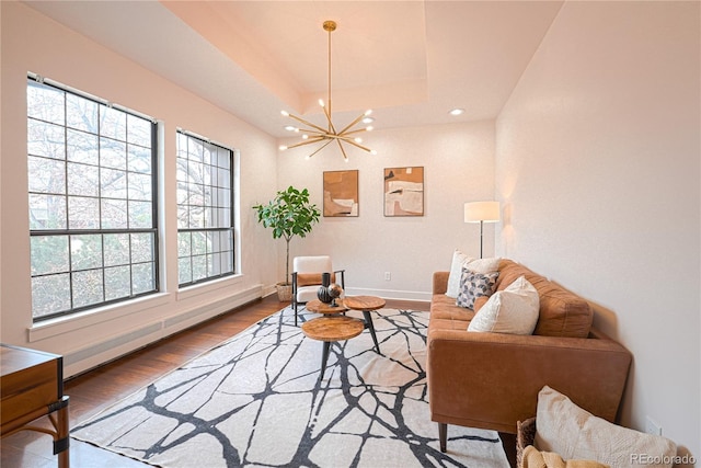 living room with a raised ceiling, baseboard heating, wood-type flooring, and an inviting chandelier