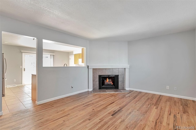 unfurnished living room featuring a tiled fireplace, a textured ceiling, and light wood-type flooring