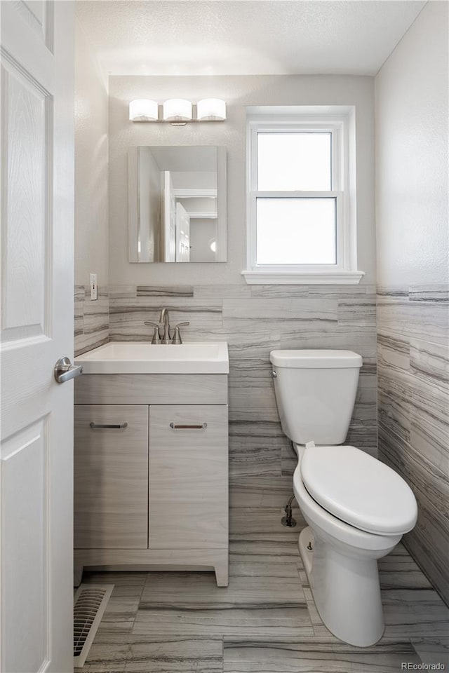 bathroom with tile walls, toilet, and vanity