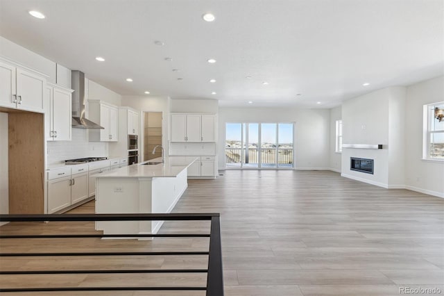 kitchen featuring stainless steel appliances, a center island with sink, white cabinets, and wall chimney exhaust hood