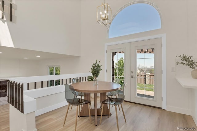 dining space featuring a high ceiling, wood finished floors, a chandelier, baseboards, and french doors