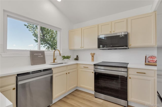 kitchen featuring stainless steel appliances, a sink, cream cabinetry, tasteful backsplash, and lofted ceiling