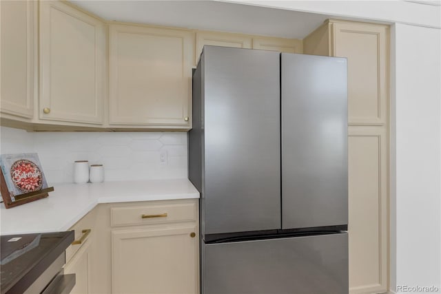 kitchen featuring freestanding refrigerator, cream cabinetry, backsplash, and light countertops