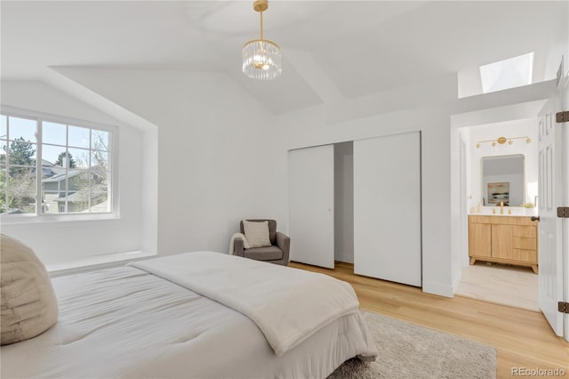 bedroom featuring lofted ceiling, light wood-type flooring, a chandelier, a closet, and connected bathroom