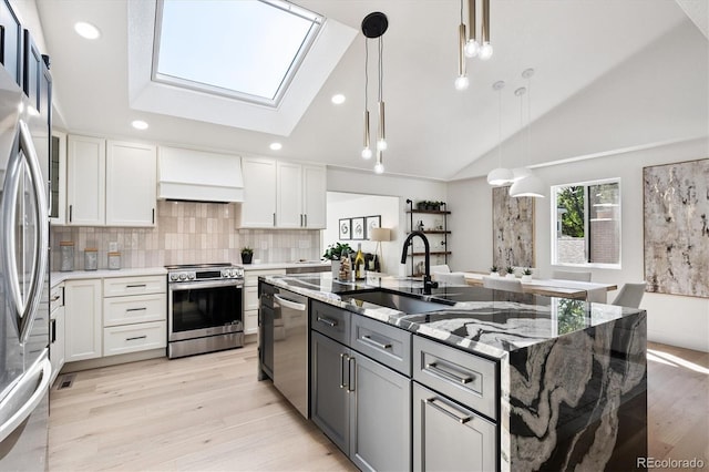 3206 S Pontiac St, Denver, CO 80224 - kitchen with appliances with stainless steel finishes, lofted ceiling, a skylight, an island with sink, and light wood-style floors
