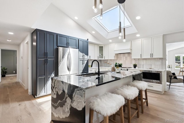 3206 S Pontiac St, Denver, CO 80224 - kitchen with a skylight, premium range hood, stainless steel refrigerator, lofted ceiling, and light wood finished floors