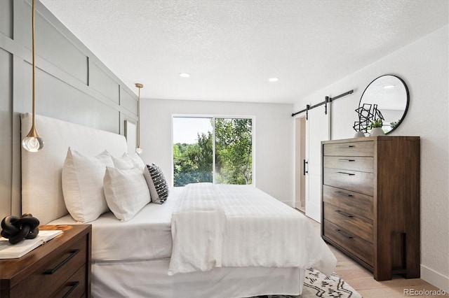 3206 S Pontiac St, Denver, CO 80224 - bedroom featuring a barn door, light wood-style flooring, recessed lighting, and a textured ceiling