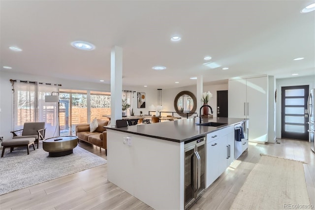 kitchen with light wood-type flooring, white cabinetry, beverage cooler, and sink