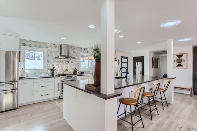 kitchen featuring stainless steel appliances, white cabinetry, a breakfast bar area, and wall chimney range hood