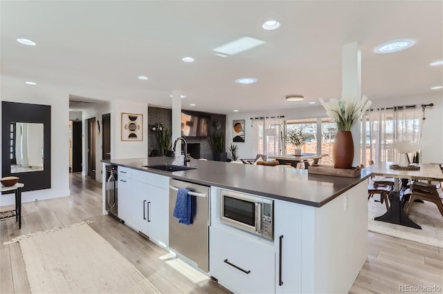 kitchen featuring a kitchen island with sink, sink, appliances with stainless steel finishes, white cabinetry, and beverage cooler