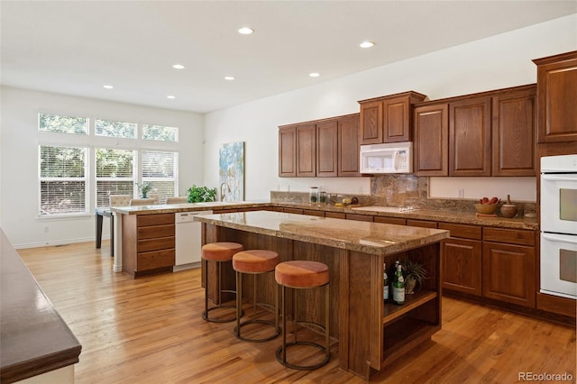 kitchen with white appliances, a center island, kitchen peninsula, and light hardwood / wood-style flooring