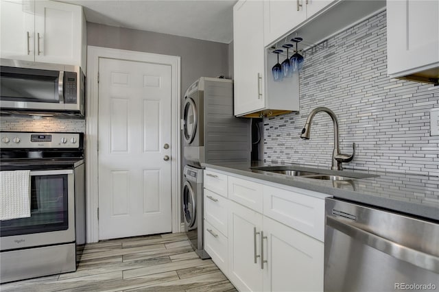 kitchen featuring tasteful backsplash, stacked washer / dryer, appliances with stainless steel finishes, white cabinets, and sink