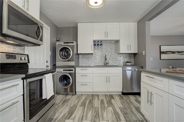 kitchen with stainless steel appliances, sink, white cabinets, stacked washer / drying machine, and backsplash